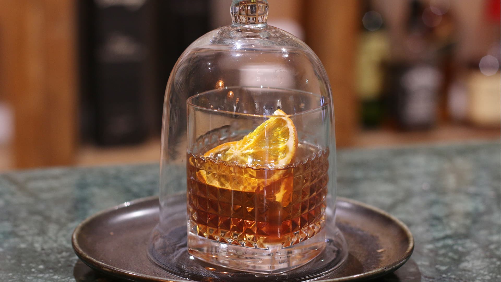 Cocktail sous cloche en verre, décoré d’orange.