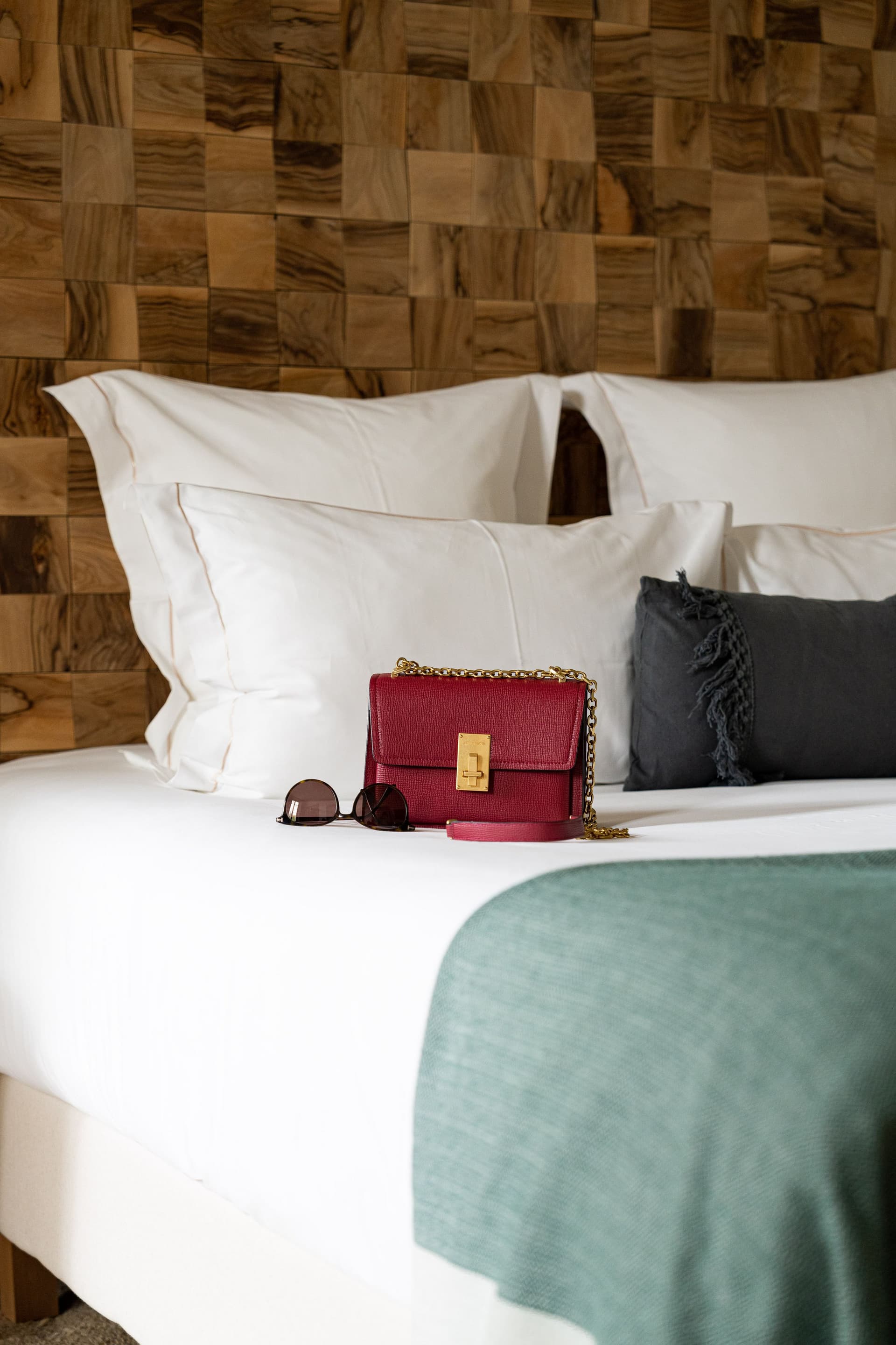 Sac rouge et lunettes sur lit blanc.