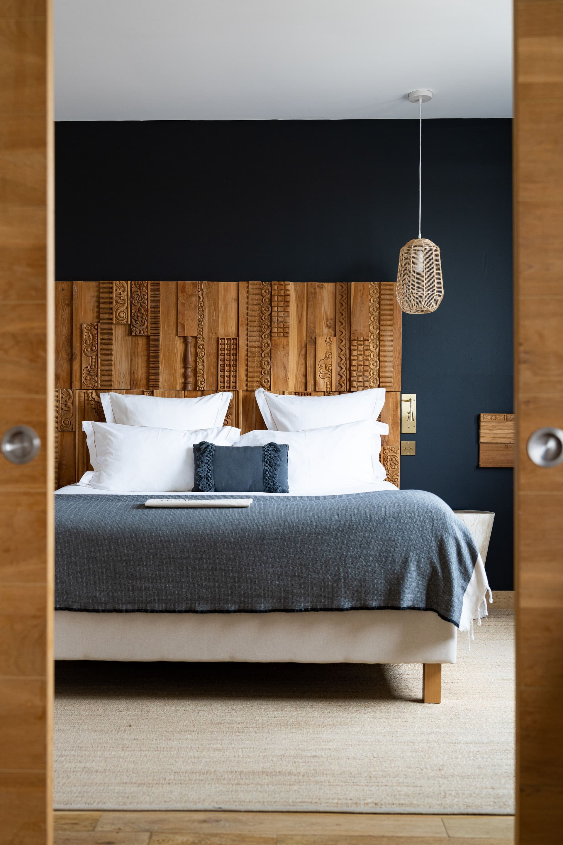 Lit avec tête en bois sculpté et lampe suspendue.