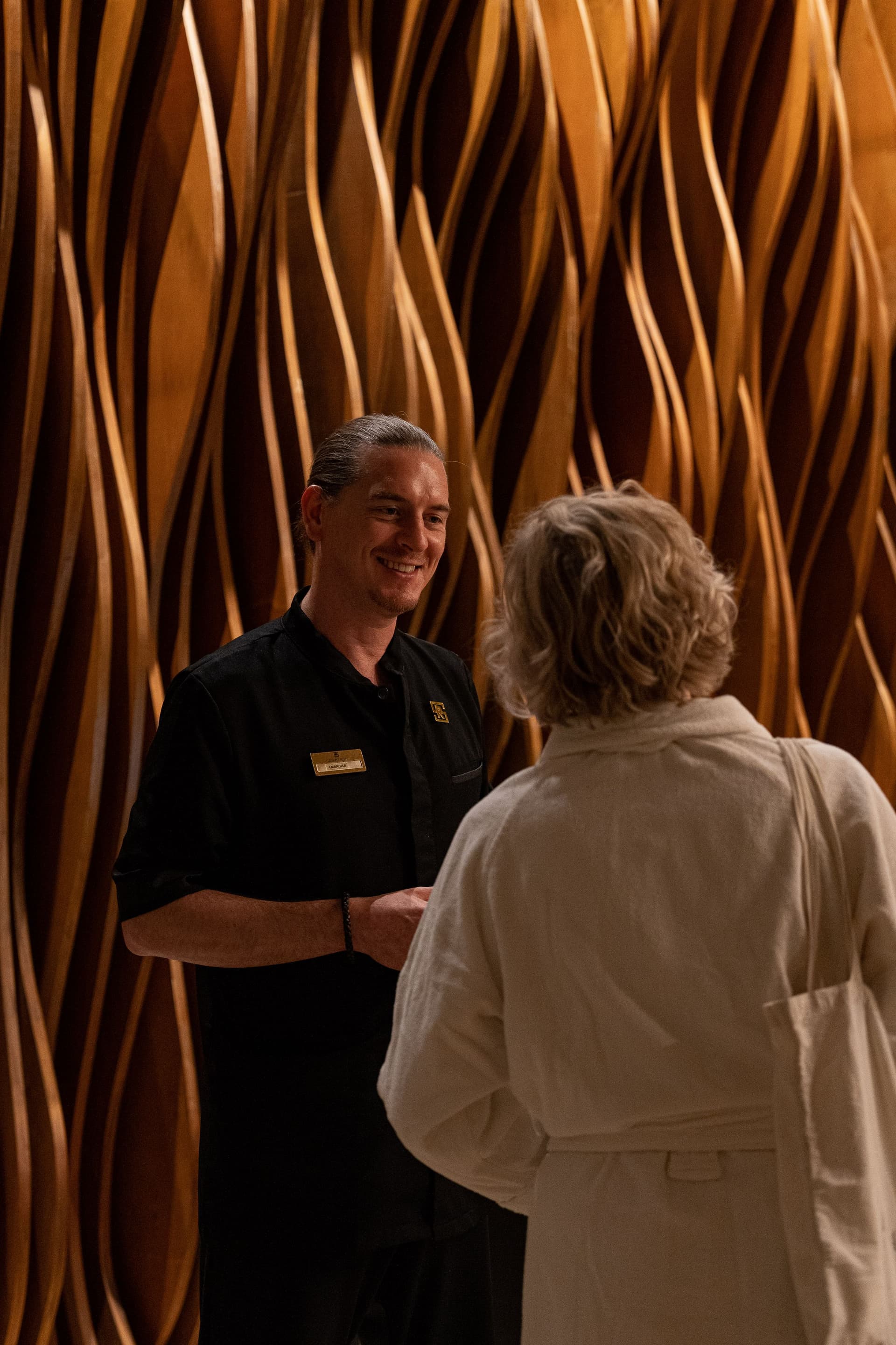 Homme souriant discutant avec femme devant mur en bois.