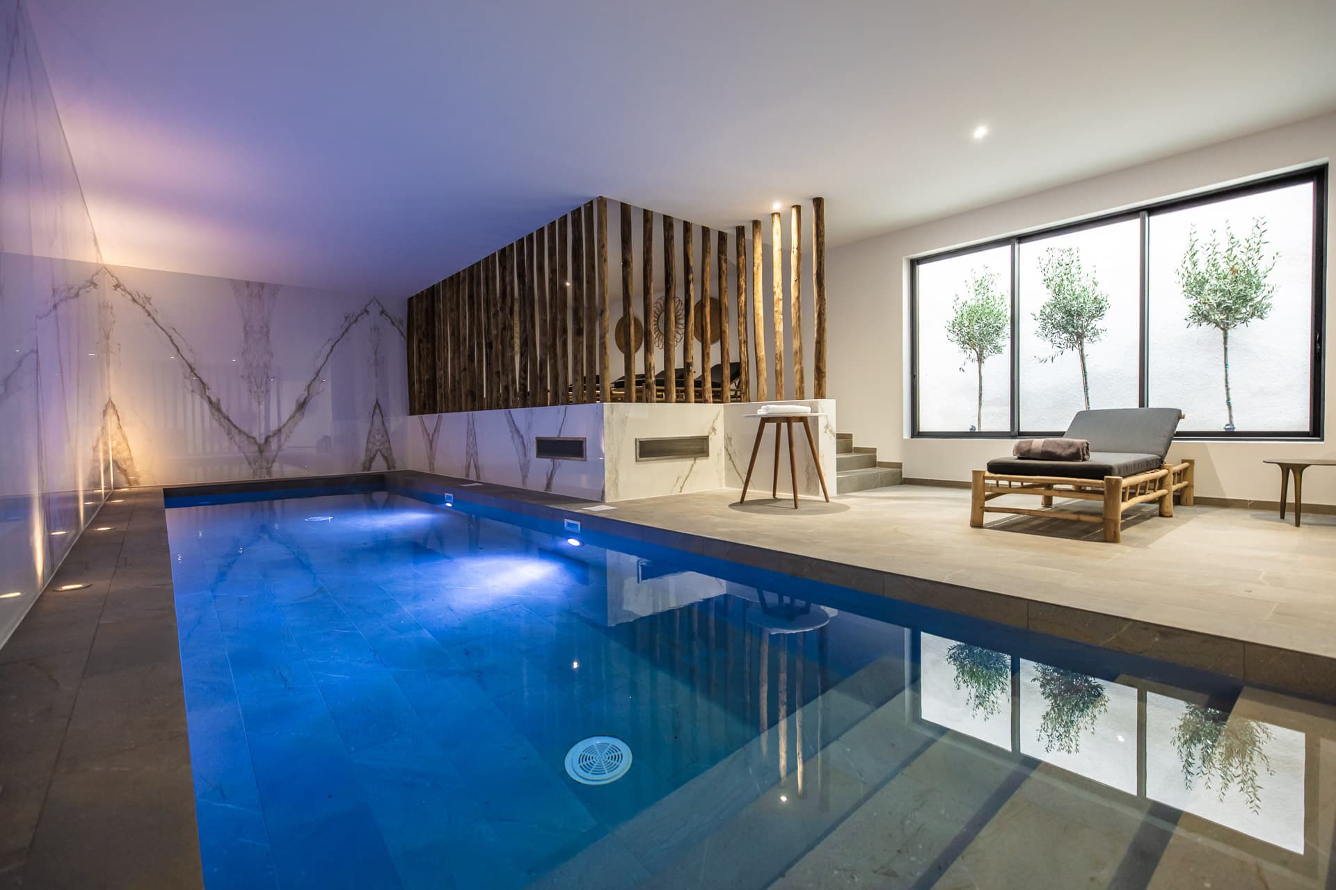 Piscine intérieure moderne avec chaise longue et arbres.