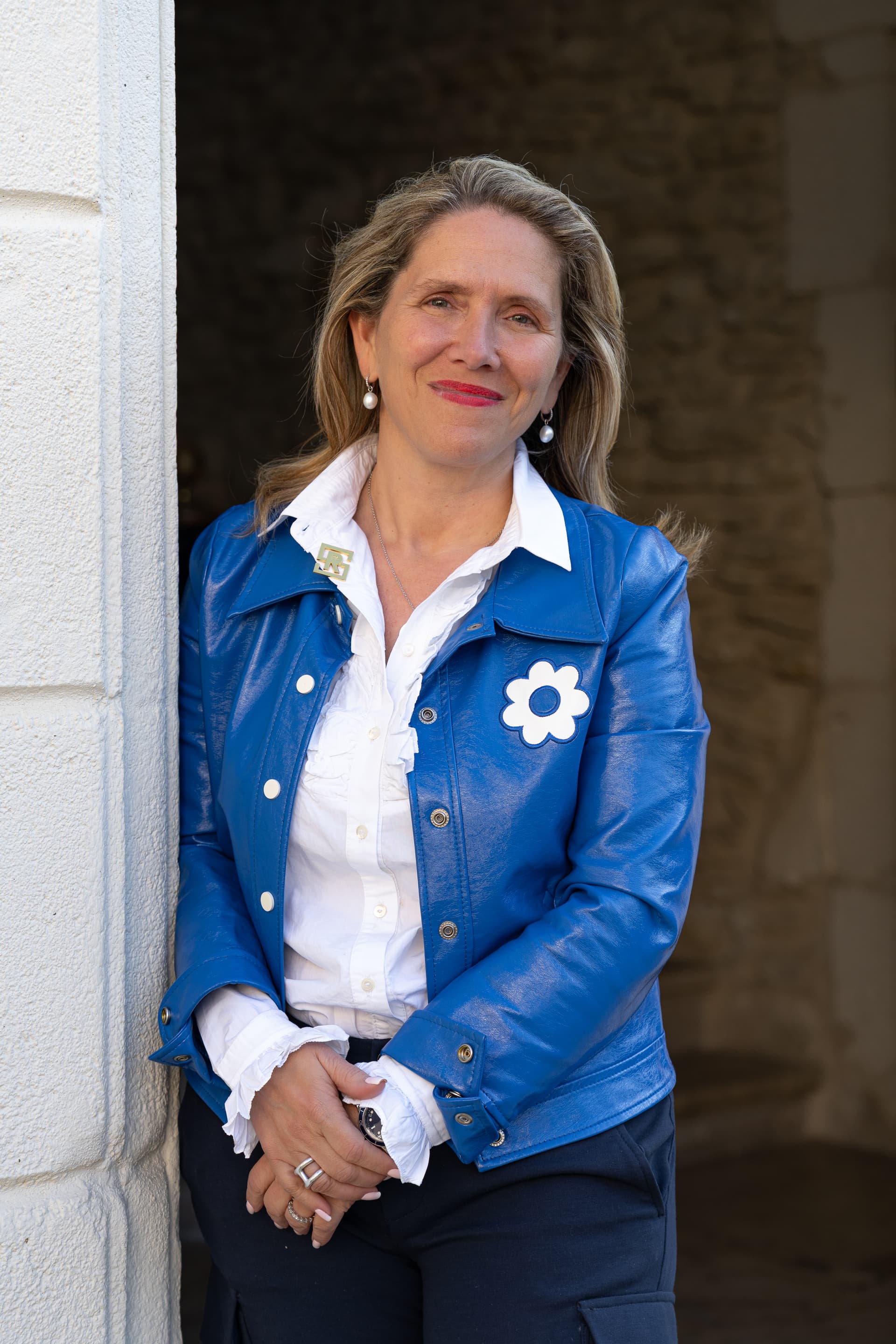 Personne souriante en veste bleue appuyée sur un mur.